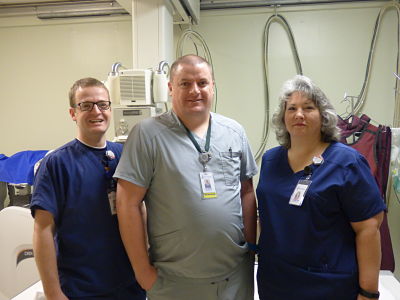 Picture of two male radiology techs and one female radiology tech standing in the x-ray room.