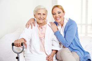 Two females sitting down, an elderly woman and a female Nurses smiling 