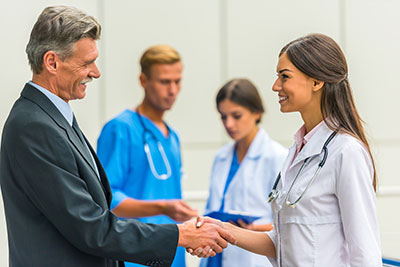 Picture of a man and female Physician shaking hands. There is a male and female nurse in the background talking. 