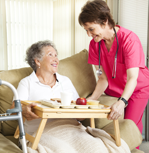 Female in home nurse bringing a female patient her breakfast on a tray 